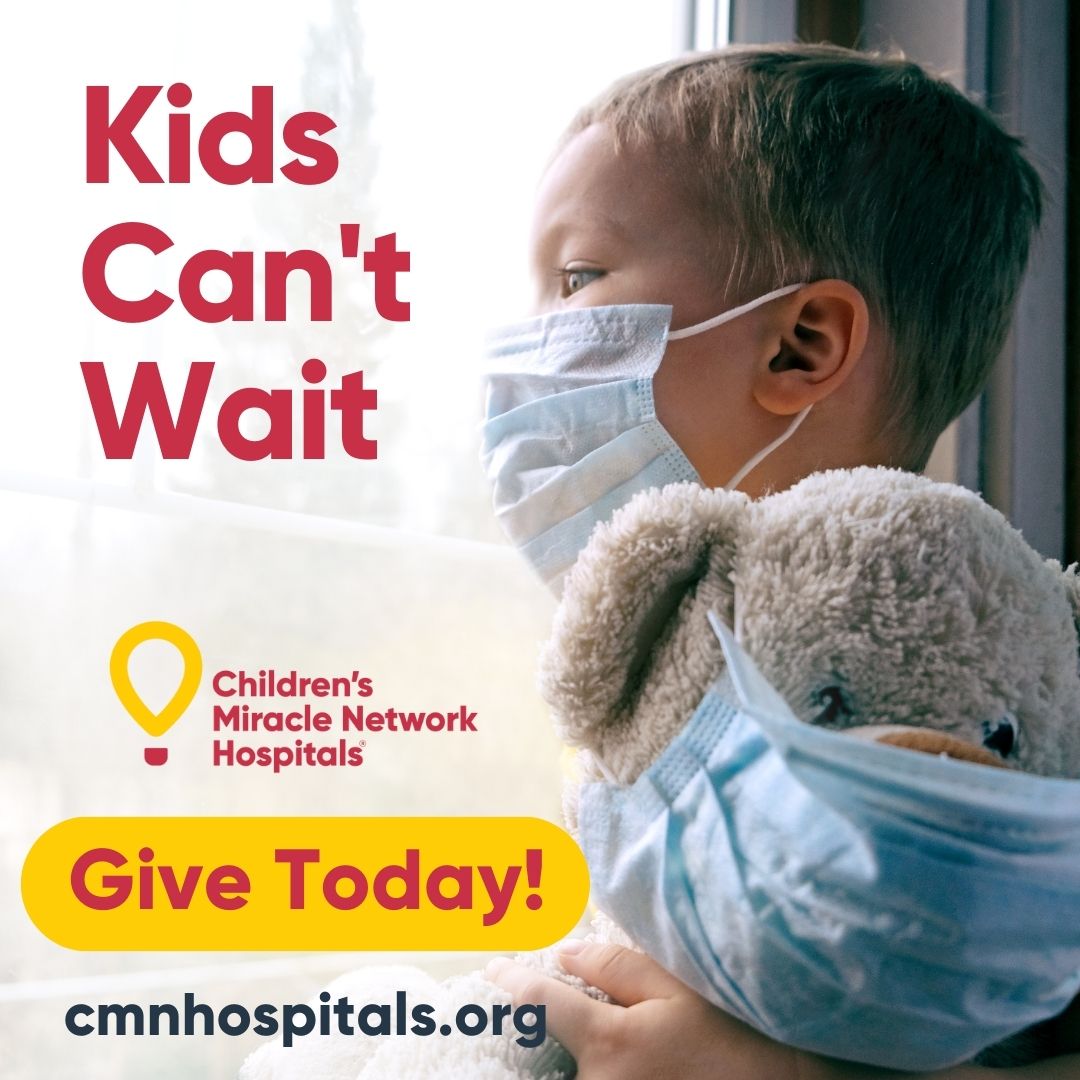 A child stands gazing out of a window with a surgical mask on.